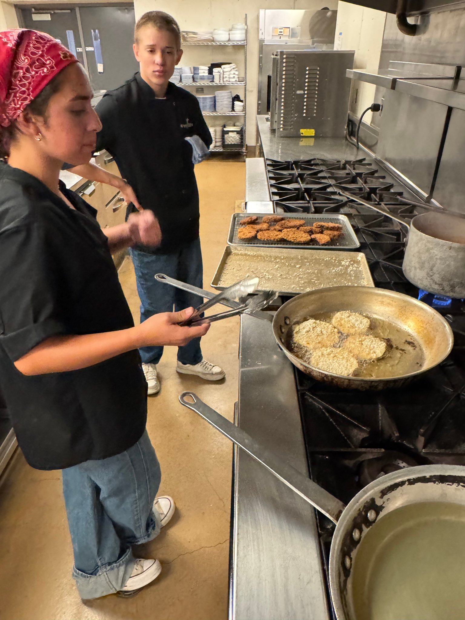 Camper frying at a commercial gas range with kitchen behind